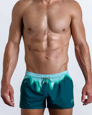 Front view of model wearing the MINT CONDITION men’s beach shorts in teal and aqua melting ice cream print by the Bang! Clothes brand of men's beachwear from Miami.