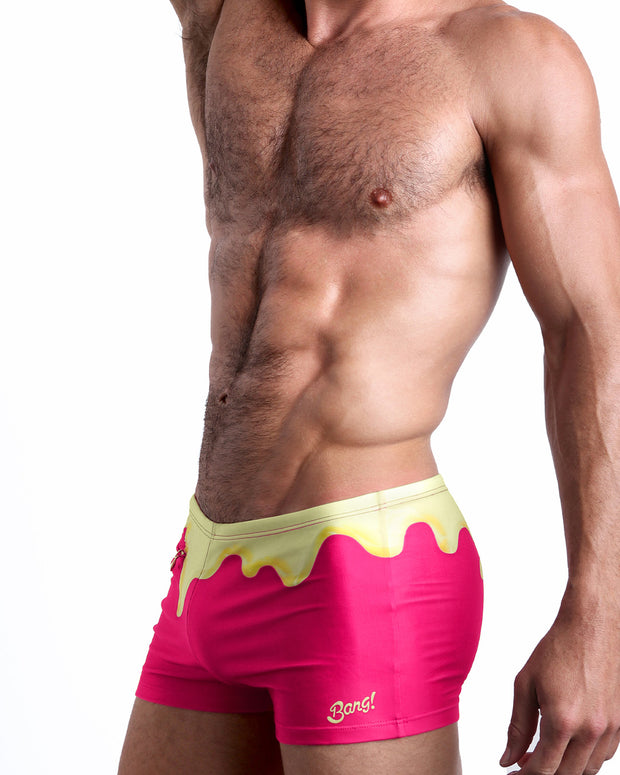 Side view of a masculine model wearing the MY MILKSHAKE compression swimwear shorts in magenta pink and a pale yellow melting ice cream print by BANG! Clothes.