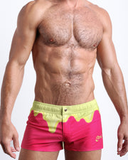 Frontal view of model wearing the MY MILKSHAKE men’s square leg swim trunks in a bright pink color featuring yellow melting ice cream print near the waist by the Bang! brand of men's beachwear from Miami.