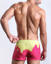 Back side view of sexy male model wearing men's MY MILKSHAKE swimwear speedo shorts featuring hot bright pink and a light yellow melting ice cream theme made by Miami based Bang brand of men's beachwear.