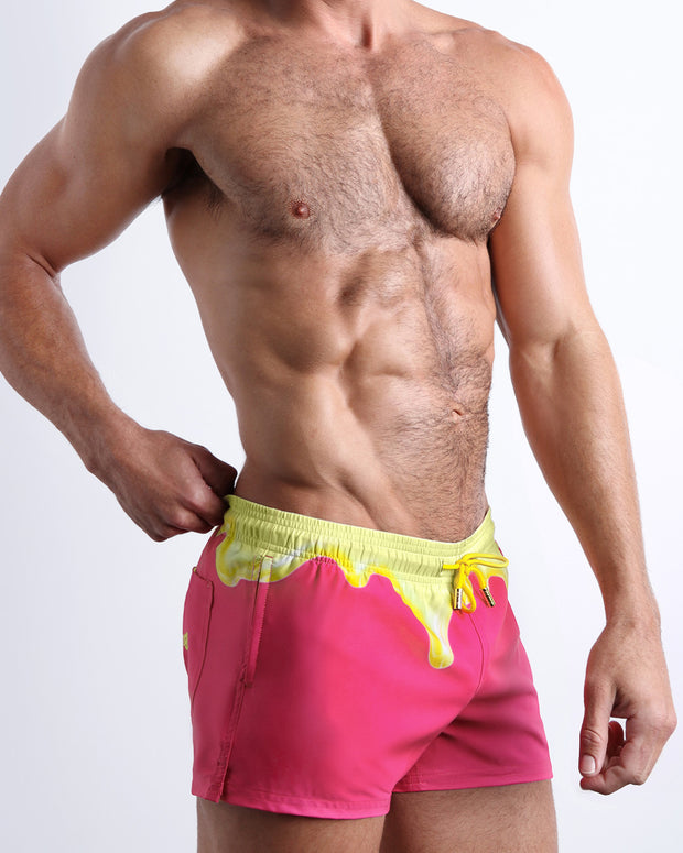 Side view of men’s shorter leg length shorts in a hot pink color with yellow melting graphic made by Miami based Bang brand of men&