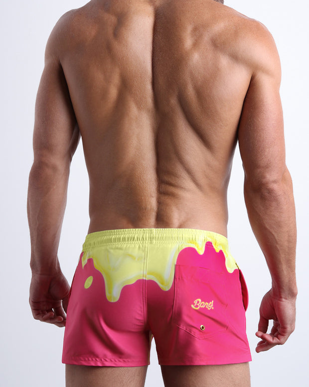 Back view of male model wearing the MY MILKSHAKE beach trunks in a bright pink color with a pale yellow melting ice cream graphic for men by BANG! Miami.