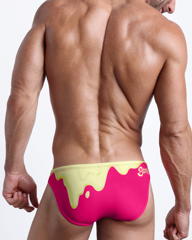 Back view of a model wearing MY MILKSHAKE men’s beach mini-brief in a hot bright pink and a light yellow melting ice cream theme made by the Bang! Miami official brand of men&