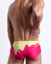 Back view of a Male model wearing Brazilian Beach Sunga Swimsuit for men in magenta pink and a pale yellow melting ice cream print by the Bang! Clothes brand of men's beachwear.