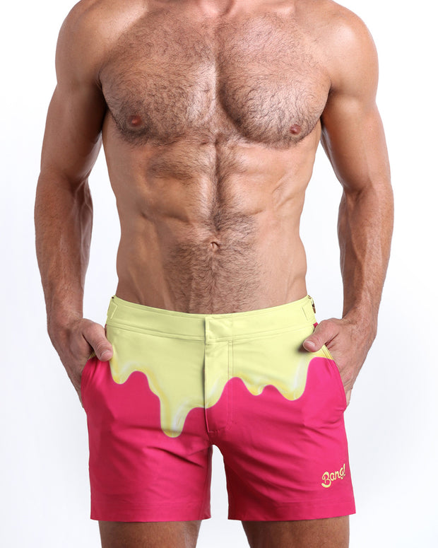 Front view of model wearing the MY MILKSHAKE men’s beach tailored shorts in a bright pink color featuring yellow melting ice cream print near the waist by the Bang! Clothes brand of men&