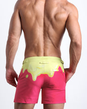 Back view of male model wearing the MY MILKSHAKE beach trunks for men by BANG! Miami in magenta pink and a pale yellow melting ice cream print
