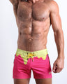 Frontal view of model wearing the MY MILKSHAKE men’s mini swimming shorts in a bright pink color featuring yellow melting ice cream print near the waist by the Bang! menswear brand.