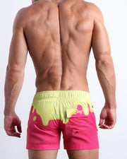 Male model's back view showing the MY MILKSHAKE swim flex shorts for men in hot bright pink and a light yellow melting ice cream theme by Bang! men's swimwear.