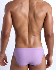 Back view of a male model wearing men’s swim briefs in neon light purple color by the Bang! Clothes brand of men's beachwear.