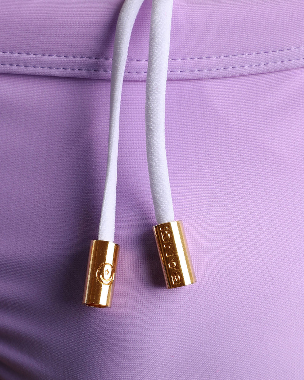 Close-up view of men’s summer swimwear by BANG! clothing brand, showing white cord with custom branded golden cord ends, and matching custom eyelet trims in gold.