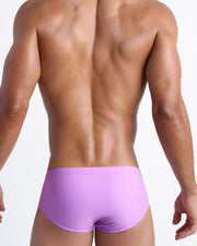 Back view of a male model wearing men’s swim sungas in neon light purple color made with Italian-made Vita By Carvico Econyl Nylon by the Bang! Clothes brand of men's beachwear.