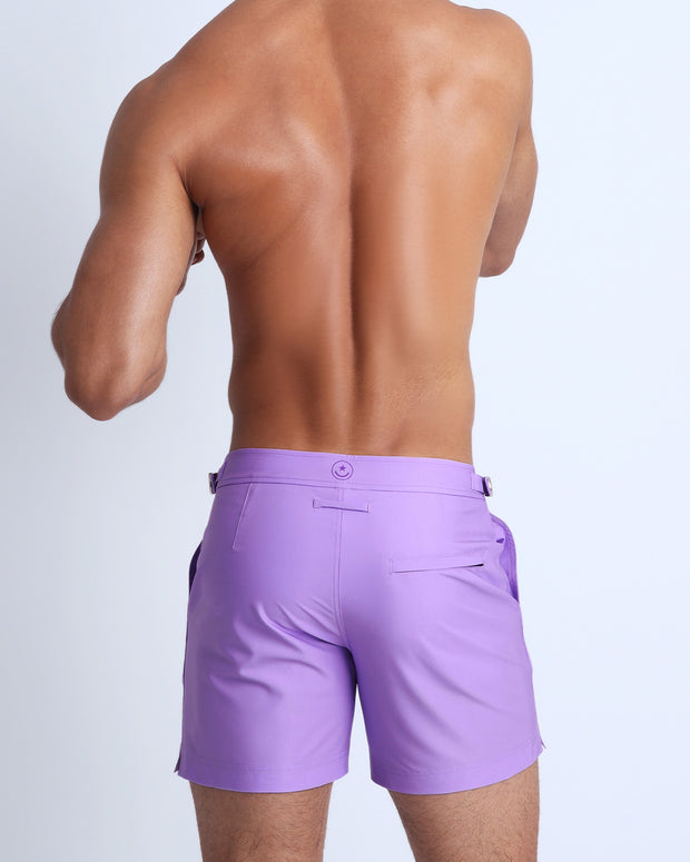 Back view of a male model wearing men’s beach trunks in a light violet by the Bang! Clothes brand of men&