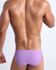 Back view of a male model wearing men’s swim mini-brief in neon light purple color made with Italian-made Vita By Carvico Econyl Nylon by the Bang! Clothes brand of men's beachwear.