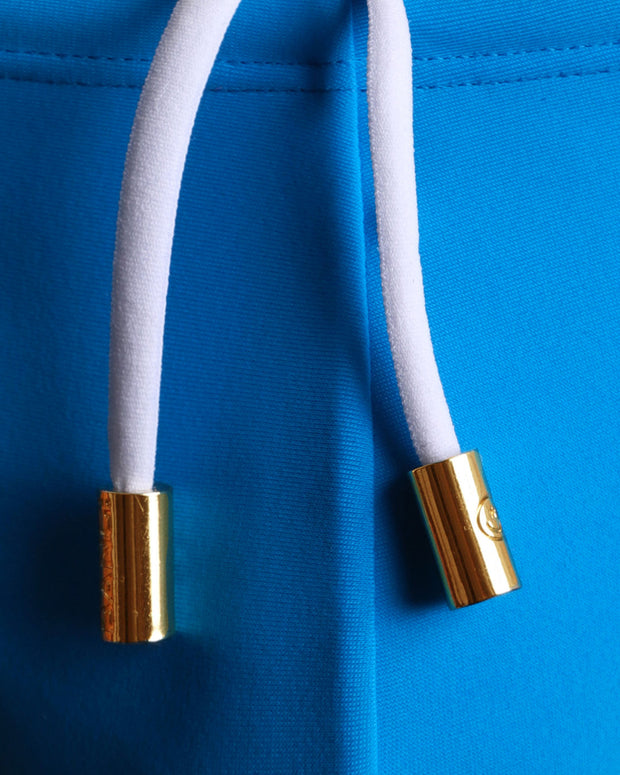 Close-up view of men’s summer swim mini brief by BANG! clothing brand, showing white cord with custom branded golden cord ends, and matching custom eyelet trims in gold.