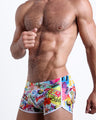 Side view of muscular male model wearing PEOPLE FROM IBIZA Summer swimsuit for the beach with palm trees, seashells, cocktails, and music graphics by BANG! Miami.