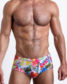 Frontal view of a sexy male model wearing men’s Brazilian Sunga swimsuit in PEOPLE FROM IBIZA in white with colorful Miami pop art designed by the Bang! Menswear brand from Miami.