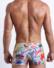 Back view of a Male model wearing swim trunks for men in white with colorful pop art inspired by sandy marton and beleares by the Bang! Clothes brand of men's beachwear.