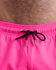 Close-up view of the PINK BOMB men’s summer shorts, showing black cord with custom branded golden cord ends, and matching custom eyelet trims in gold.