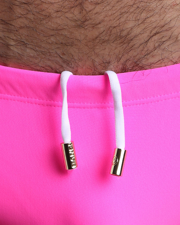 Close-up view of the PINK BOMB Swim Sunga mens swimsuit a bright pink color with white internal drawstring cord showing custom branded golden buttons by BANG! clothing brand.