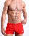 Frontal view of a sexy male model wearing the PRIME RED men’s square leg swim trunks in a bright red color by the Bang! Menswear brand from Miami.