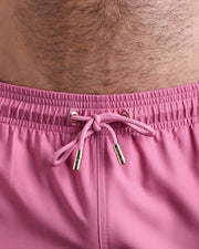 Close-up view of the ROSA MEXICANO men’s summer shorts, showing pink cord with custom branded golden cord ends, and matching custom eyelet trims in gold.