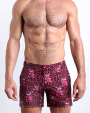 Front view of model wearing the STARSTRUCK men’s beach tailored shorts in a red berry color with black BANG! Typography print and tiger pop art by the Bang! Clothes brand of men's beachwear from Miami.