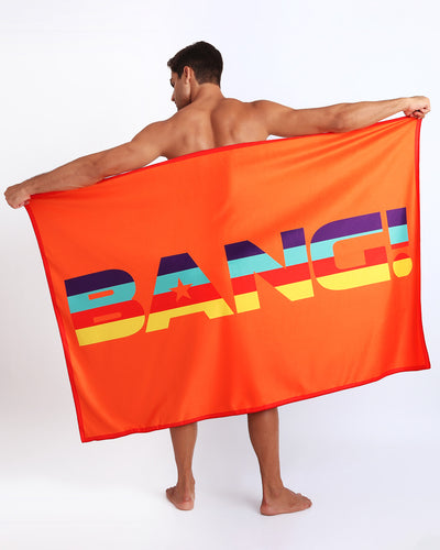 Model showing the STRIPE'A'POSE REMIX quick-dry microfiber towel with matching swim briefs for the beach in bright orange with color stripes. 