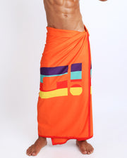 Model showing the STRIPE'A'POSE REMIX quick-dry microfiber towel with matching swim briefs for the beach in bright orange with color stripes. 