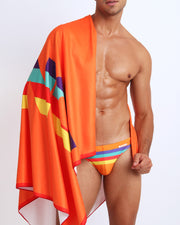 Frontal view of sexy male model showing the STRIPE'A'POSE REMIX unisex lightweight towel in a hot orange color with color stripes in yellow, bold red, aqua, and purple by Bang! Clothing from Miami.