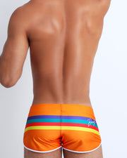Back view of male model wearing swim shorts in orange color with color stripes in aqua blue, bold red, yellow and dark blue.