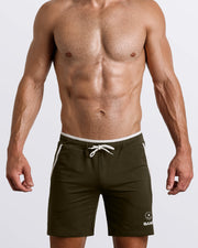 Frontal view of male model wearing the TACTICAL GREEN athletic crossfit gym shorts in a solid forest green color by the Bang! brand of men's beachwear from Miami.