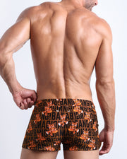 Back side view of sexy male model wearing men's TIGER HEARTS swimwear speedo shorts in brown with orange tigers holding a heart pop art artwork made by Miami based Bang brand of men's beachwear.