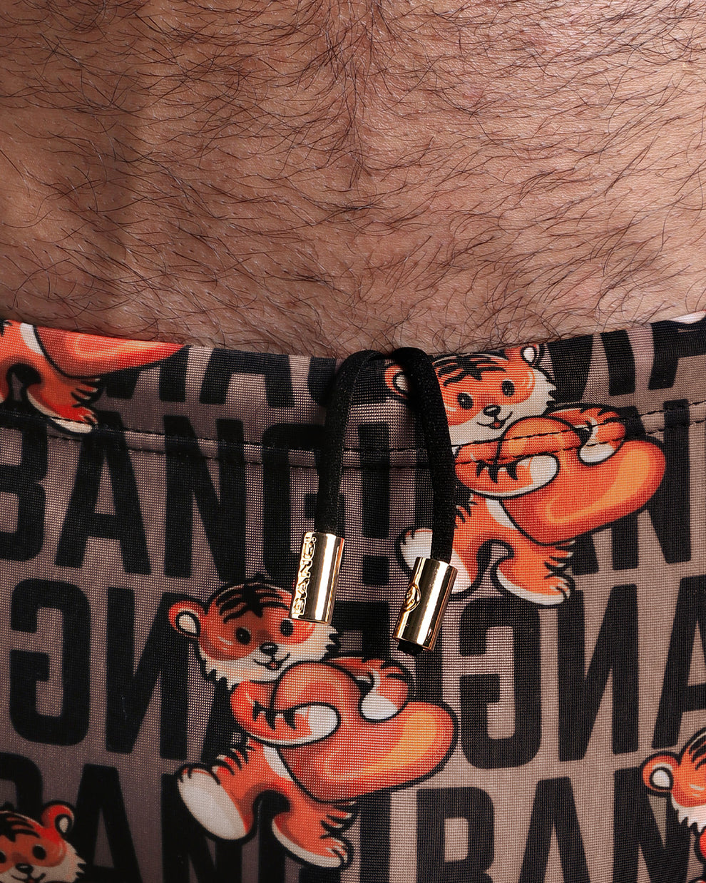 Close-up view of the TIGER HEARTS Swim Sunga mens swimsuit in brown with orange tigers holding a heart love pop art artwork with an internal drawstring cord in white showing custom branded golden buttons by BANG! clothing brand.