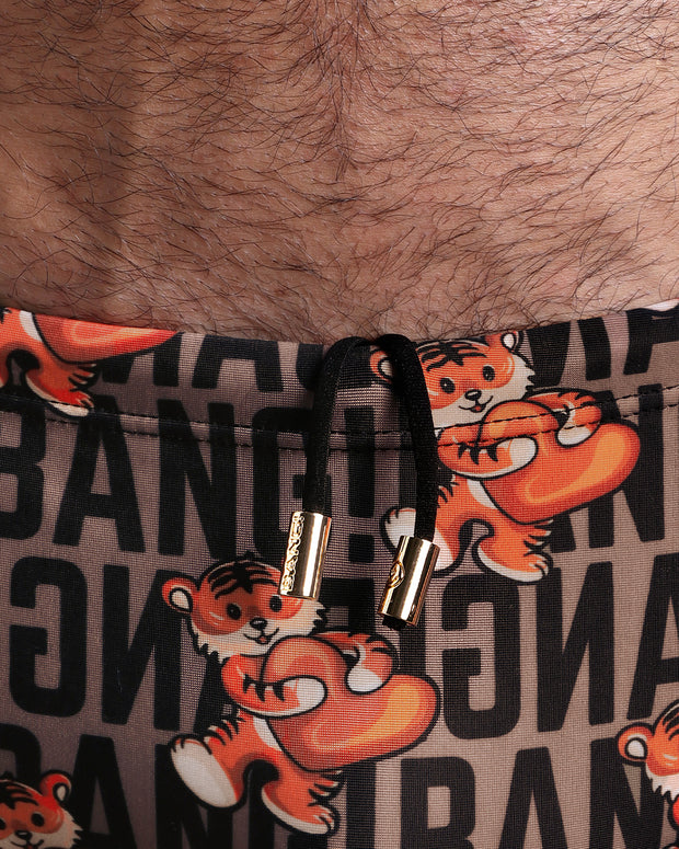Close-up view of the TIGER HEARTS Swim Sunga mens swimsuit in brown with orange tigers holding a heart love pop art artwork with an internal drawstring cord in white showing custom branded golden buttons by BANG! clothing brand.