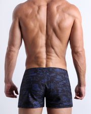 Back view of male model wearing the TOILE DE MIAMI (BLACK/BLUE) beach shorts for men by BANG! Miami featuring a black and navy blue toile de jouy print.