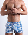 Front view of model wearing the TOILE DE MIAMI (BLUE) men’s beach shorts in white with sky blue Toile De Jouy art by the Bang! Clothes brand of men's beachwear from Miami.