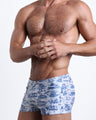 Side view of a masculine model wearing the TOILE DE MIAMI (BLUE) compression swimwear shorts in white with blue Miami inspired artwork by BANG! Clothes.