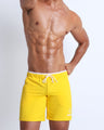 Frontal view of male model wearing the solid TONED YELLOW  athletic crossfit gym shorts by the Bang! brand of men's beachwear from Miami.