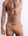 Male model wearing the TOP TAN men’s swim shorts in a beige cream color by the Bang! brand of men's beachwear from Miami.