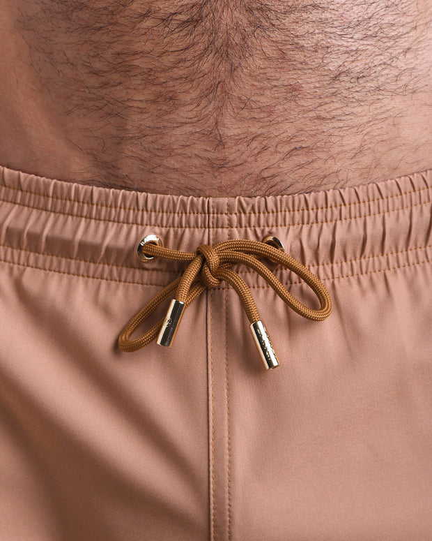 Close-up view of the TOP TAN men’s summer shorts, showing brown cord with custom branded golden cord ends, and matching custom eyelet trims in gold.