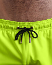 Close-up view of the ULTRA NEON men’s summer show shorts, showing black cord with custom branded golden cord ends, and matching custom eyelet trims in gold.