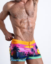 Side view of an in-shape male model wearing UNDER A NEON SKY mini shorts for men featuring a colorful Miami inspired artwork made by the Miami-based Bang! brand of men's beachwear.
