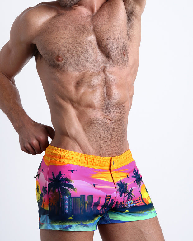 Side view of an in-shape male model wearing UNDER A NEON SKY mini shorts for men featuring a colorful Miami inspired artwork made by the Miami-based Bang! brand of men&