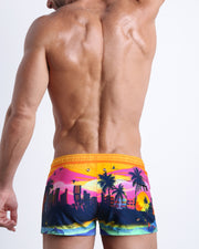 Back side view of sexy male model wearing men's UNDER A NEON SKY swimwear speedo shorts in a pop color with the miami sunset skyline made by Miami based Bang brand of men's beachwear.