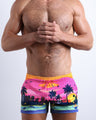 Front view of model wearing the UNDER THE NEON SKY men’s beach shorts in pink & orange sunset skyline print by the Bang! Clothes brand of men's beachwear from Miami.