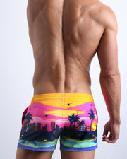 Back view of male model wearing the UNDER THE NEON SKY beach trunks in a Miami skyline print for men by BANG! Miami.