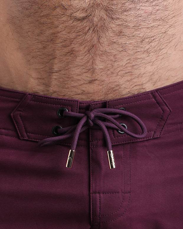 Close-up view of men’s summer beach shorts by BANG! clothing brand, showing dark purple cord with custom branded golden cord ends, and matching custom eyelet trims in gold.