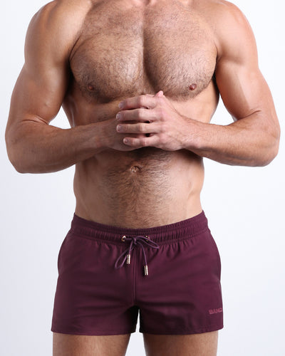 Male model wearing the VERY BERRY men’s swim shorts in dark burgundy color by the Bang! brand of men's beachwear from Miami.