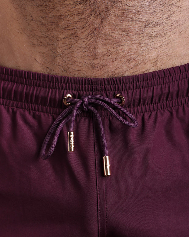 Close-up view of the VERY BERRY men’s summer shorts, showing dark purple cord with custom branded golden cord ends, and matching custom eyelet trims in gold.