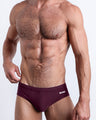 Frontal view of a sexy male model wearing the VERY BERRY Swim Brief men’s swimsuit in dark burgundy red color by the Bang! Menswear brand from Miami.